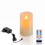 Die wiederaufladbare LED-Wachskerze mit beweglicher Flamme (D 7,5 x 12,5 cm, warmweiß) strahlt realistisch neben einem schwarzen Netzadapter und einer weißen Fernbedienung mit bunten Tasten.