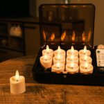 Een set van 12 3D oplaadbare LED-thee/waxinelichtjes (tot 400 uur, IP68 waterdicht, timerfunctie) en een afstandsbediening worden getoond in een open zwarte opbergdoos op een houten tafel, met één kaarsje apart buiten de doos.