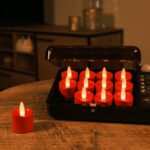 Twaalf LED-kaarsjes rood oplaadbaar 175 uur - waterdicht- met afstandsbediening (12 stuks) staan op te laden in een zwarte case op een houten tafel, één rode kaars ligt uit elkaar. De sfeervolle woonkamer is dim verlicht.