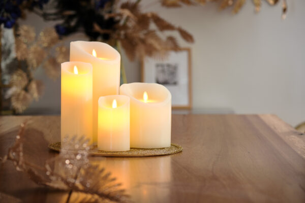De LED wax kaarsen set 4 kaarsen warm wit oplaadbaar DORSETTO gloeit warm op een houten tafel, uitgestald op een gouden dienblad met decoratieve bladeren, en creëert een gezellige en feestelijke sfeer.