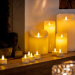 Een Oplaadbare LED wax kaars met bewegende vlam D 7,5 X 12,5 CM - warm wit gloeit warm op een houten schoorsteenmantel en geeft een gezellig en uitnodigend tintje bij de open haard en bloemdecoratie.