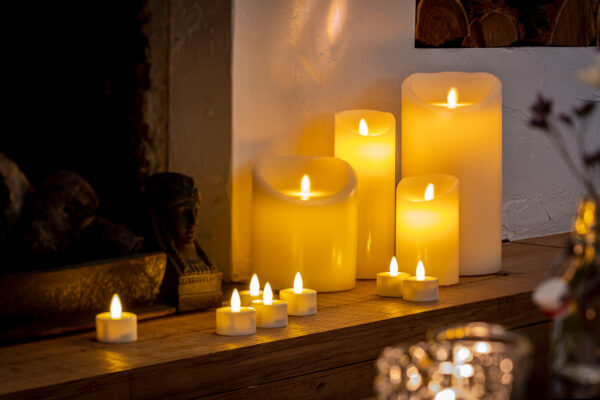 Een Oplaadbare LED wax kaars met bewegende vlam D 7,5 X 12,5 CM - warm wit gloeit warm op een houten schoorsteenmantel en geeft een gezellig en uitnodigend tintje bij de open haard en bloemdecoratie.