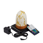 De Tafellamp DORSETTO oplaadbaar 105 uur, een ovale waterdichte lamp in marmer goud met afstandsbediening, staat op een zwarte plaat naast een oplader en een meerkleurige afstandsbediening.