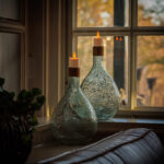 Op een vensterbank staan twee glazen vazen met daarop 3D oplaadbare LED-thee/waxinelichtjes 175 uur (set van 6, met afstandsbediening en timerfunctie) die zacht oplichten als het zonlicht naar binnen stroomt; een plant en een deel van een bank zijn vlakbij zichtbaar.