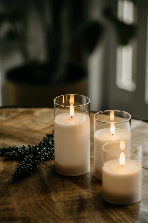 De DORSETTO led kaarsen set - oplaadbaar 105 uur met 3D vlam en afstandsbediening brandt op een houten oppervlak, naast een dennentak, en zorgt met de zachte achtergrond voor een warme, gezellige sfeer.