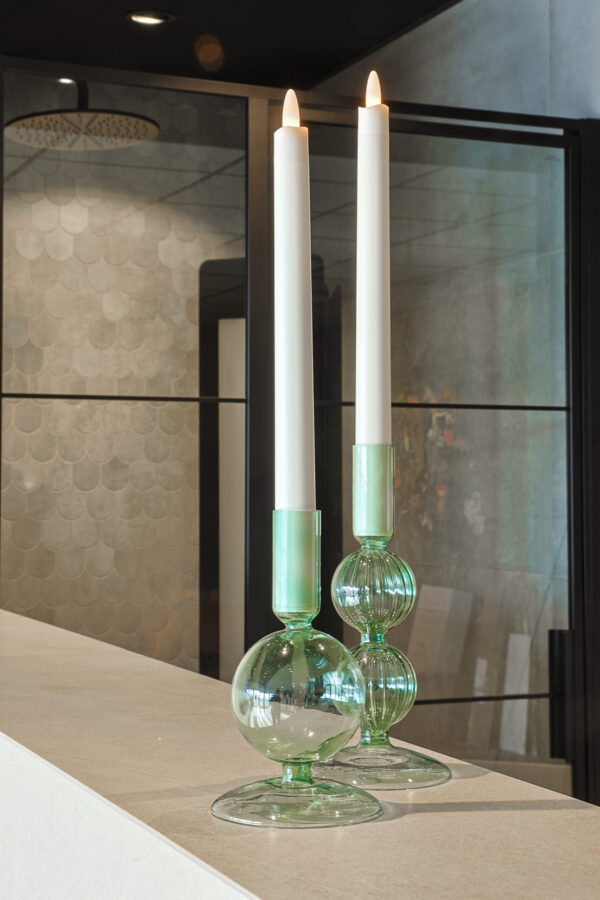 Twee LED dinerkaars 270mm oplaadbaar (130 uur warm wit, 6 stuks met afstandsbediening) in groene glazen houders gloeien warm op een licht aanrechtblad en versterken het moderne interieur met glazen panelen en betegelde wanden.