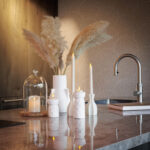 Een modern aanrecht met witte vazen van pampagras, gestapelde tijdschriften en een Dinerkaars 197mm LED DORSETTO oplaadbaar 130 uur warm wit (12-pak met afstandsbediening) kaars. Warme verlichting creëert een knus gevoel bij de strakke kraan.