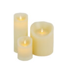 De LED wax kaarsen set 3 kaarsen warm wit oplaadbaar DORSETTO bevat drie crèmekleurige, vlamloze kaarsen van verschillende hoogtes met realistisch gloeiende vlammen, samen weergegeven tegen een witte achtergrond.