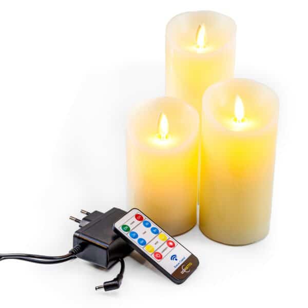 Drie Oplaadbare LED waxinekaarsen van 3 stuks DORSETTO staan met een afstandsbediening en voedingsadapter op een wit oppervlak. Deze kaarsen hebben een realistisch vlameffect en stralen een warmgeel licht uit.