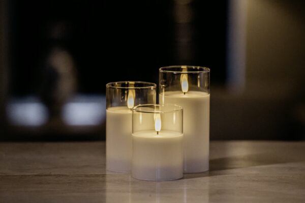 De DORSETTO LED kerzen set - oplaadbaar 105 uur met 3D vlam en afstandsbediening brandt sfeervol dichtbij elkaar in glazen houders op een egale ondergrond, tegen een zacht vervaagde donkere achtergrond.