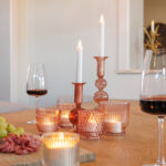 Een houten gedekte tafel met warmwitte oplaadbare LED-waxine/theelichtjes (12 stuks, 175 uur brandtijd, waterdicht, met afstandsbediening) in roze glazen houders, rode wijnglazen en een schotel met druiven en gesneden vlees creëert een gezellige eetvibe.