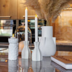 Witte keramische vazen en kandelaars met Dinerkaars 197mm LED DORSETTO oplaadbaar 130 uur warm met 12 stuks met afstandsbediening zijn gerangschikt op een marmeren aanrecht met gedroogd pampagras, waardoor een gezellige, moderne decor scène ontstaat.
