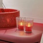 Twaalf oplaadbare LED-kaarsjes rood, waterdicht en met afstandsbediening en timerfunctie, verspreiden zacht licht op een roze oppervlak naast een rode terrazzo wastafel, wat zorgt voor een warme en gezellige sfeer.