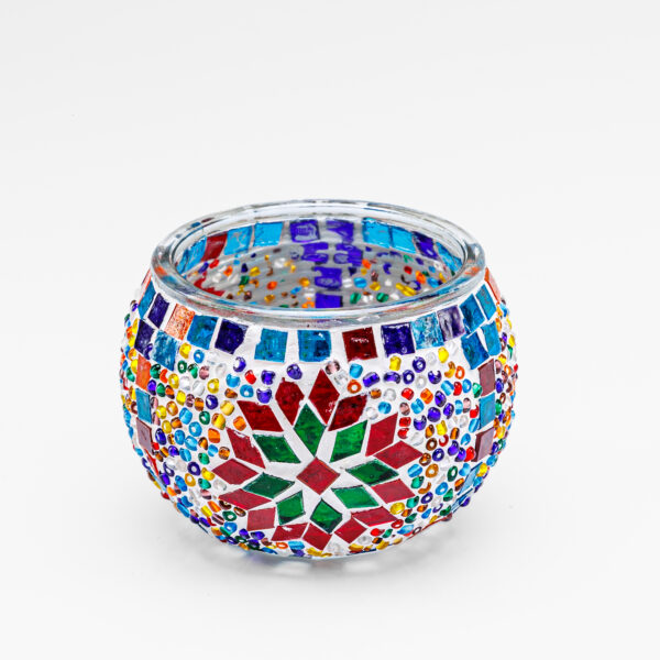 De Theelichthouder vrolijke 9 CM DORSETTO is een ronde glazen kandelaar met kleurrijke mozaïekpatronen met rode, groene, blauwe, oranje en gele geometrische vormen en stippen op een effen witte achtergrond.