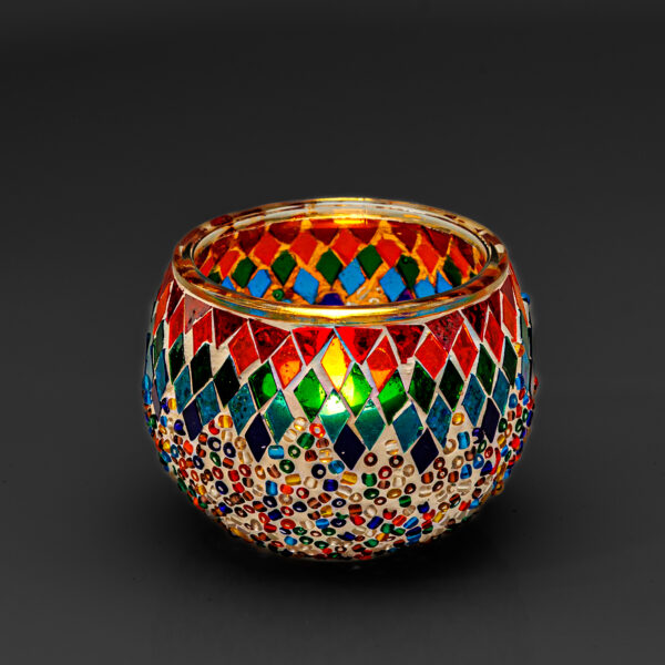 Theelichthouder gekleurde spikkels 9 CM DORSETTO: een ronde glazen kandelaar versierd met kleurrijke ruitvormige mozaïeken en veelkleurige kralen tegen een effen donkere achtergrond.