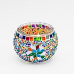 Waxinelichthouder 9 CM Dorsetto regenboog: Een kandelaar van helder glas versierd met kleurrijke mozaïekkralen en een centrale ster, met levendige rode, blauwe, groene, oranje en gele geometrische patronen.