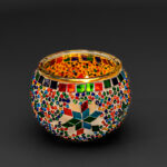 Een ronde, kleurrijke Waxinelichthouder 9 CM Dorsetto regenboog glazen kandelaar versierd met mozaïekpatronen, veelkleurige tegeltjes en een centraal sterontwerp tegen een zwarte achtergrond.