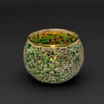 De Theelichthouder DORSETTO 9 cm donker groen is een ronde, decoratieve glazen kandelaar met een mozaïek van groene en gouden stukjes op een donkere achtergrond.