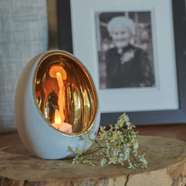 Een set van 6 LED waxinelichtjes 3D kaarsen (brandtijd 175 uur, oplaadbaar, afstandsbediening & timer) gloeit in een ronde wit met gouden houder op hout, met kleine witte bloemen en een ingelijste zwart-wit foto op de achtergrond.