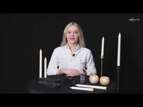 Een vrouw met lang blond haar zit aan een zwarte tafel versierd met witte kaarsen en de LED dinerkaars oplaadbaar 150 mm 58 uur warm wit (6 stuks met afstandsbediening). Ze draagt een helder wit overhemd tegen een zwarte achtergrond.