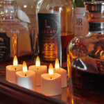 Een close-up van drankflessen, waaronder Jack Daniels en VSOP cognac, op een houten oppervlak met zes 3D oplaadbare LED-thee/waxinelichtjes (175 uur, met afstandsbediening en timerfunctie) die ervoor oplichten.