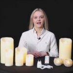 Een vrouw in een wit shirt zit aan een tafel met de DORSETTO LED wax kaarsen set 4 kaarsen warm met oplaadbaar, afstandsbediening en voedingsadapter tegen een zwarte achtergrond.