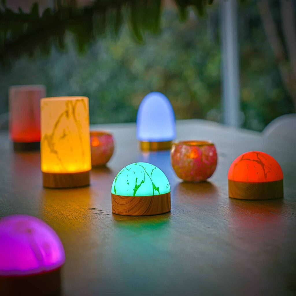 De oplaadbare Tafellamp DORSETTO (105 uur), ovaal en waterdicht in marmer wit met grijze houtlook, ligt op een buitentafel; de lampen zijn sfeervol gerangschikt met groen op de achtergrond.