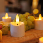 led theelichtjes op accu gloeit warm op een houten oppervlak naast druiven en ander fruit, terwijl 3D oplaadbare LED-thee/waxinelichtjes (175 uur, afstandsbediening, 6 stuks, timerfunctie) de achtergrond zachtjes verlichten voor een gezellige sfeer.