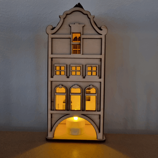 De Waxinelichthouder houten huis DORSETTO is een klein houten model met boogramen en een gebogen dak, van binnenuit verlicht door een LED waxinelichtje en ontworpen om op een plat oppervlak tegen een gewone muur te staan.