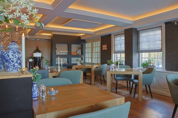 Een gezellig, modern restaurant met houten tafels, zachtgroene stoelen, warme verlichting en grote ramen heeft een elegante inrichting met vazen, planten en LED-Teelicht wiederaufladbar mit Fernbedienung für 175 Stunden Brenndauer.