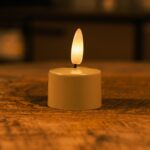 Een kleine LED-kaars op batterijen met een warme, gloeiende vlam staat op een houten oppervlak en creëert een gezellige sfeer met zachte verlichting.