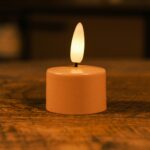 Een kleine LED-kaars op batterijen met een warme gele vlam staat op een houten oppervlak en creëert een gezellige sfeer.