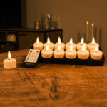 Ein Satz batteriebetriebener Teelichter mit realistisch flackernden Flammen ist auf einem Holztisch aufgestellt. Daneben befindet sich eine Fernbedienung. Im Hintergrund ist ein gemütlicher, sanft beleuchteter Raum zu sehen.