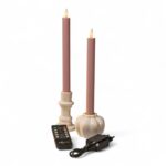 Zwei rosafarbene LED-Kerzen in weißen Haltern, eine Fernbedienung und ein schwarzer Stromadapter sind auf einem weißen Hintergrund angeordnet.