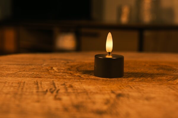 Twaalf Oplaadbare waxinelichtjes zwart met een brandduur tot 400 uur en afstandsbediening staan op een houten oppervlak en werpen een warme gloed. De zacht vervaagde achtergrond creëert een gezellige, ontspannen sfeer.