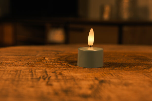 Een set van 12 olivijngroene LED waxinelichtjes met afstandsbediening staat op een houten oppervlak, werpt een warme, zachte gloed voor maximaal 400 uur en creëert een gezellige, intieme sfeer met zijn zachte licht.