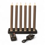 Sechs batteriebetriebene braune Kerzen mit flammenförmigen Spitzen sind in einem schwarzen rechteckigen Ständer angeordnet. Davor befinden sich eine Fernbedienung mit beschrifteten Tasten und ein schwarzer Stromadapter mit Kabel.