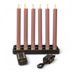 Sechs rosafarbene elektronische Kegelkerzen mit kleinen flammenförmigen Lichtern sind aufrecht in einem schwarzen rechteckigen Halter angeordnet. Davor befinden sich eine Fernbedienung und ein schwarzes Netzteil mit Kabel, alles auf weißem Hintergrund.
