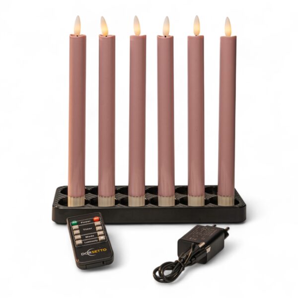 Sechs rosafarbene elektronische Kegelkerzen mit kleinen flammenförmigen Lichtern sind aufrecht in einem schwarzen rechteckigen Halter angeordnet. Davor befinden sich eine Fernbedienung und ein schwarzes Netzteil mit Kabel, alles auf weißem Hintergrund.