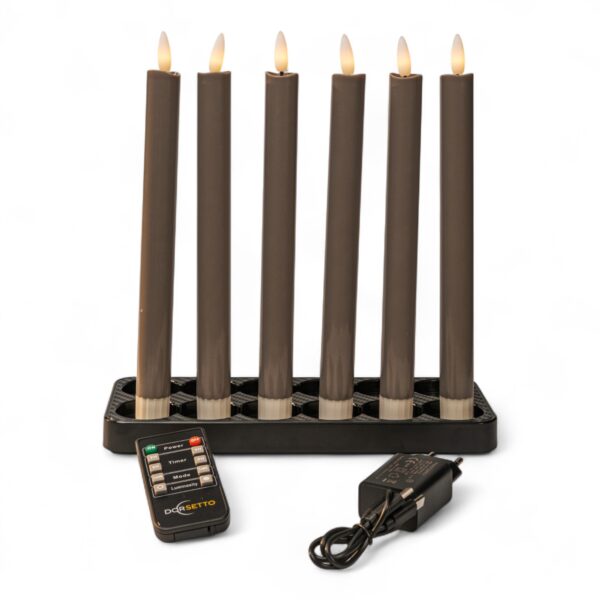 Sechs hohe, graue elektronische Kerzen mit brennenden Spitzen sind in einem schwarzen rechteckigen Halter angeordnet. Vor dem Halter befinden sich eine Fernbedienung und ein schwarzer Stromadapter, alles vor einem weißen Hintergrund.