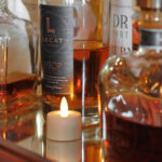 Wasserfeste, wiederaufladbare LED-Teelichter (12 Stück, warmweiß, bis zu 400 Std. Brenndauer, inkl. Fernbedienung) sorgen auf einem reflektierenden Untergrund neben Whiskey- und Cognacflaschen für eine gemütliche Atmosphäre.