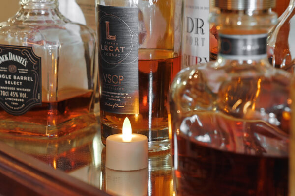 Wasserfeste, wiederaufladbare LED-Teelichter (12 Stück, warmweiß, bis zu 400 Std. Brenndauer, inkl. Fernbedienung) sorgen auf einem reflektierenden Untergrund neben Whiskey- und Cognacflaschen für eine gemütliche Atmosphäre.