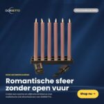 Das 6er-Set LED-Stabkerzen in Rosa (250 mm), wiederaufladbar, dimmbar und mit Fernbedienung, wird auf schwarzem Sockel vor dunklem Hintergrund präsentiert. Ein "Shop nu" Button und niederländischer Text sind sichtbar.