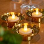 Zwölf wasserfeste, wiederaufladbare LED-Teelichter (warmweiß, bis zu 400 Std. Brenndauer, inkl. Fernbedienung) sorgen in goldenen Haltern auf Holz für ein elegantes und gemütliches Ambiente.