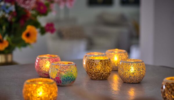 Auf einem Tisch neu arrangiert, erzeugen LED-Teelichter wiederaufladbar mit Fernbedienung ein warmes, gemütliches Licht. Im Hintergrund sorgen bunte Blumen für dekorative Akzente in dieser einladenden Szene.