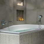 In einer grau gefliesten Ecke steht eine moderne Badewanne mit strukturierten Kacheln. Darüber befinden sich zwei Regale mit wiederaufladbaren LED-Teelichtern (12 Stück, warmweiß, wasserdicht), die mit bis zu 400h Laufzeit und Fernbedienung ein gemütliches Ambiente schaffen.