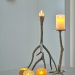 Zwei LED-Wachskerzen D12,5 × H15 CM (warmweiß, wiederaufladbar, mit Fernbedienung) stehen auf einer Fläche neben drei kleinen beleuchteten Glasvotiven in einem minimalistischen modernen Interieur.